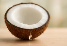 Olejek kokosowy na skórę – właściwości i zastosowanie Symboliczna kropla olejku kokosowego wypływająca z kokosa