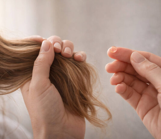 Kobieta trzymająca włosy, w kontekście ich wypadania - obok kropla suplementu (symbolicznie)