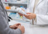 Farmaceuta trzymający lek i pacjent przy ladzie w kontekście zmieniania dawki leku