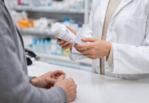 Farmaceuta trzymający lek i pacjent przy ladzie w kontekście zmieniania dawki leku