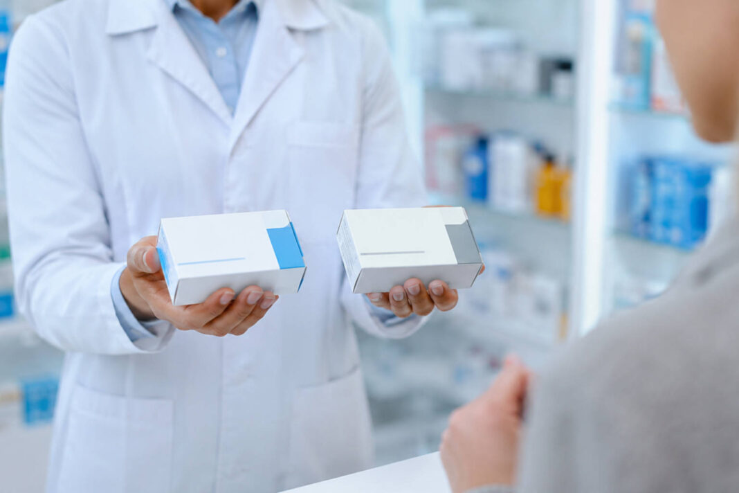 Farmaceuta trzymający w dłoniach dwa leki - oryginalny i generyczny. Grafika bez marek